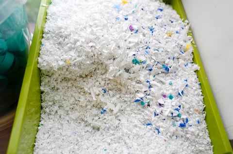 Clean white shredded plastic flakes in green bin for quality control