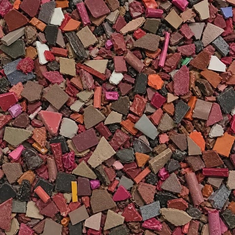 Scattered fragments of crushed eyeshadow and makeup in shades of pink, burgundy, brown, orange, and black