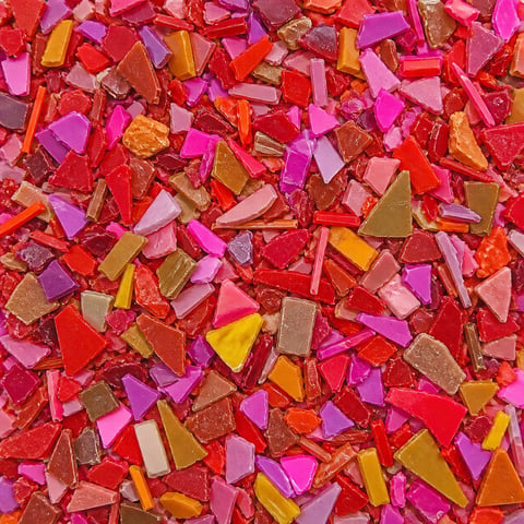 Colorful scattered candy pieces in red, pink, yellow, and gold tones filling the entire frame