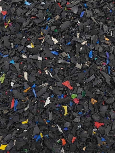 Overhead view of shredded black plastic waste with colorful scattered fragments in blue, red, yellow, and white