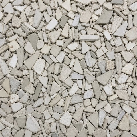 Overhead view of irregular light gray and white stone or concrete chips scattered across a surface