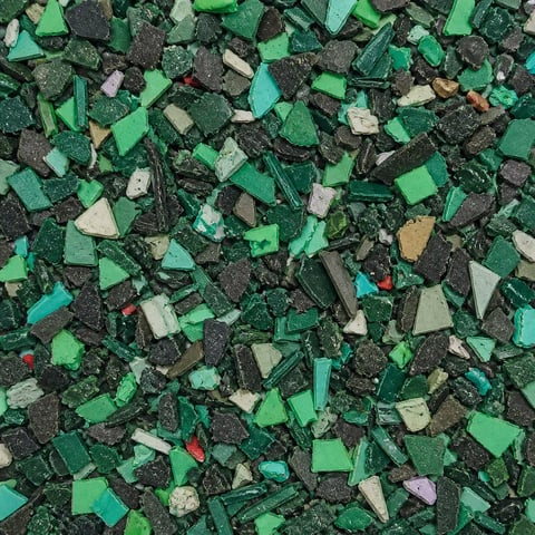 Overhead view of shredded plastic waste and debris in various shades of green, black, and tan mixed together