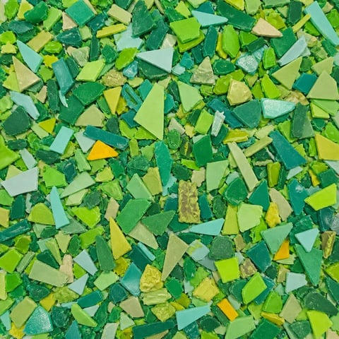Scattered green and yellow paper or foam pieces in various shades, forming an abstract textured background pattern