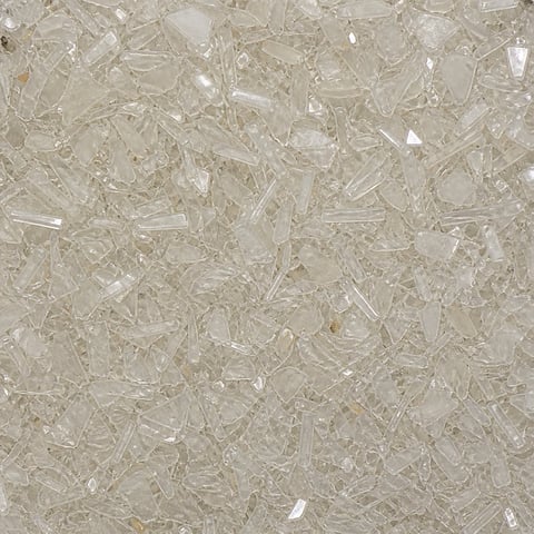 Close-up of crushed clear glass or transparent stone aggregate material with jagged fragments scattered across a textured surface